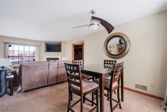 dining space with baseboards, visible vents, light colored carpet, ceiling fan, and a fireplace