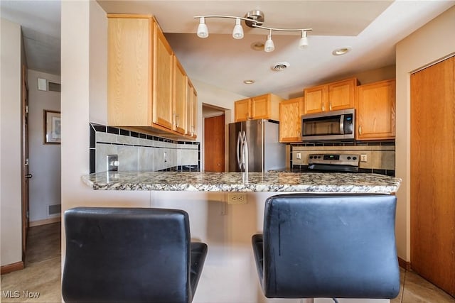 kitchen with baseboards, visible vents, a peninsula, stainless steel appliances, and backsplash