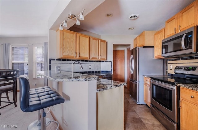 kitchen with a breakfast bar area, visible vents, appliances with stainless steel finishes, light brown cabinets, and a peninsula