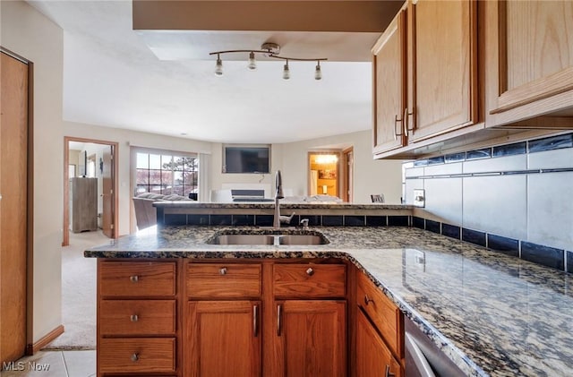 kitchen featuring brown cabinetry, open floor plan, a sink, dark stone counters, and a peninsula