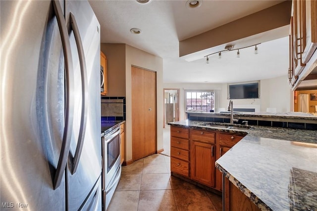 kitchen featuring light tile patterned floors, decorative backsplash, appliances with stainless steel finishes, brown cabinetry, and a sink