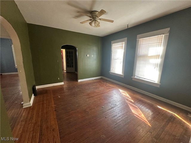 empty room featuring a ceiling fan, baseboards, arched walkways, and hardwood / wood-style floors