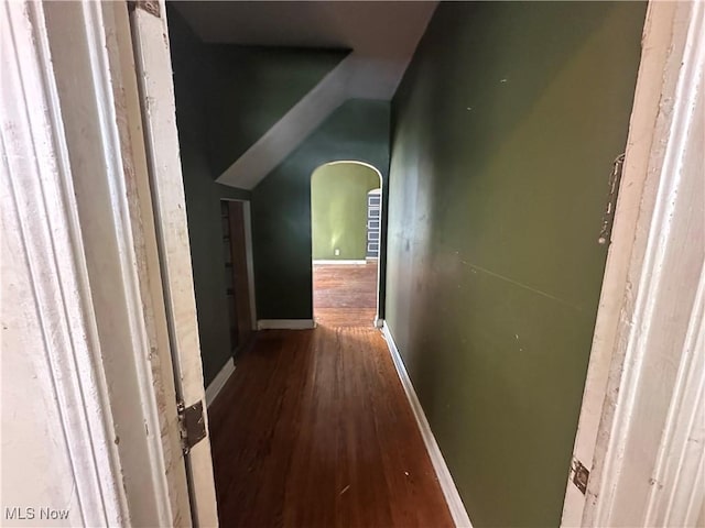 hall with lofted ceiling, arched walkways, baseboards, and wood finished floors