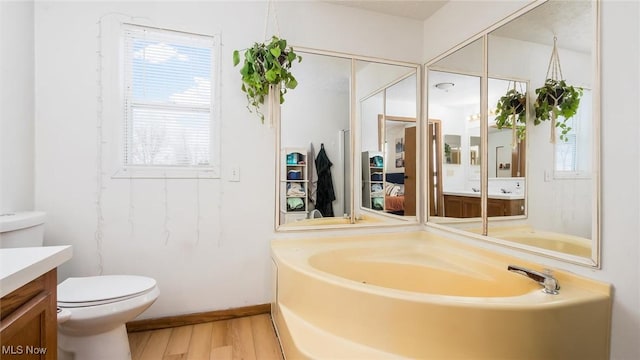 full bathroom featuring plenty of natural light, toilet, wood finished floors, vanity, and a bath