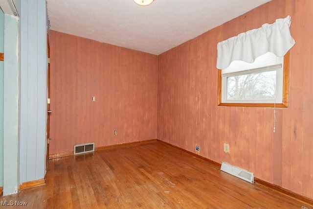 spare room featuring wood walls, wood-type flooring, visible vents, and baseboards