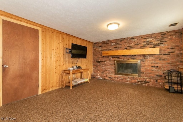 unfurnished living room featuring wooden walls, visible vents, carpet, a textured ceiling, and a brick fireplace