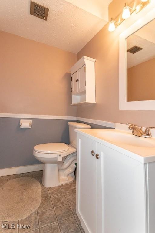 half bathroom with a textured ceiling, tile patterned flooring, toilet, visible vents, and vanity