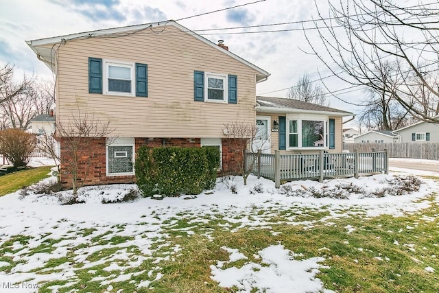 tri-level home with a chimney, fence, and brick siding