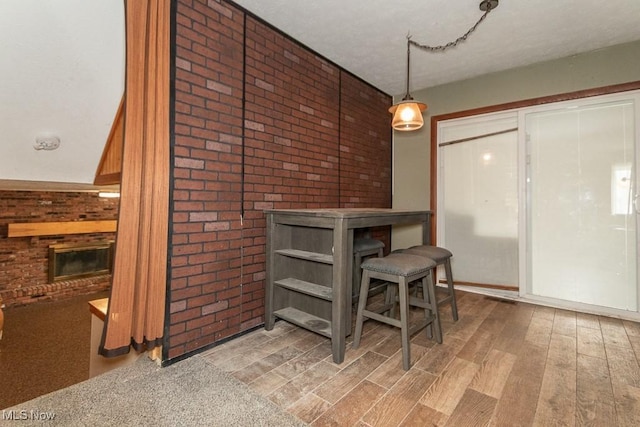 dining space with light wood-type flooring, a brick fireplace, and brick wall