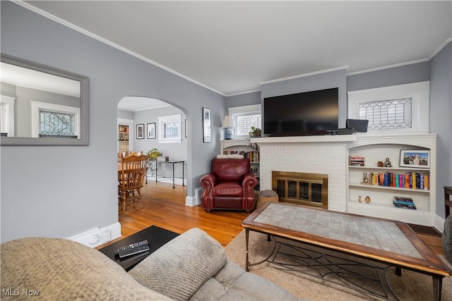 living room featuring arched walkways, a fireplace, wood finished floors, baseboards, and crown molding