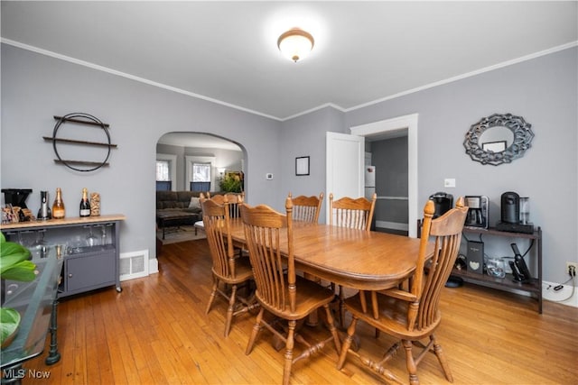 dining space with light wood-style floors, visible vents, arched walkways, and ornamental molding