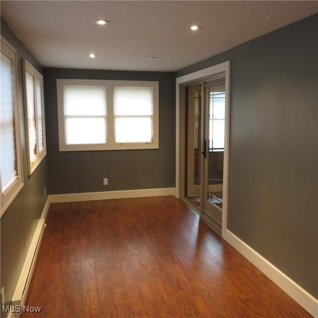 empty room with a baseboard heating unit, recessed lighting, wood finished floors, and baseboards