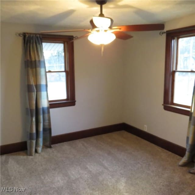 carpeted spare room with a ceiling fan and baseboards