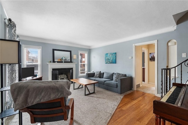 living area featuring stairs, a textured ceiling, a fireplace, and wood finished floors