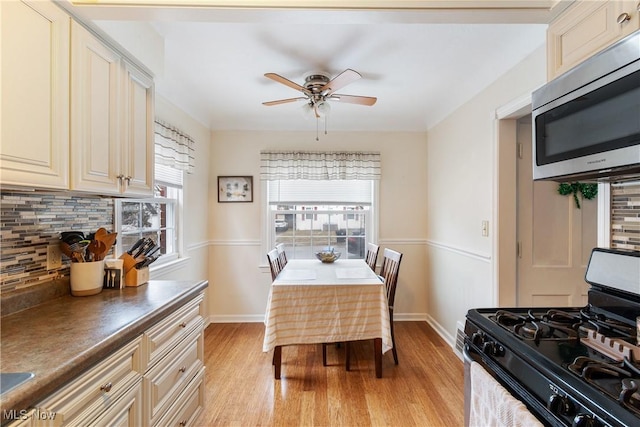 kitchen featuring cream cabinetry, stainless steel microwave, backsplash, light wood-style floors, and gas stove