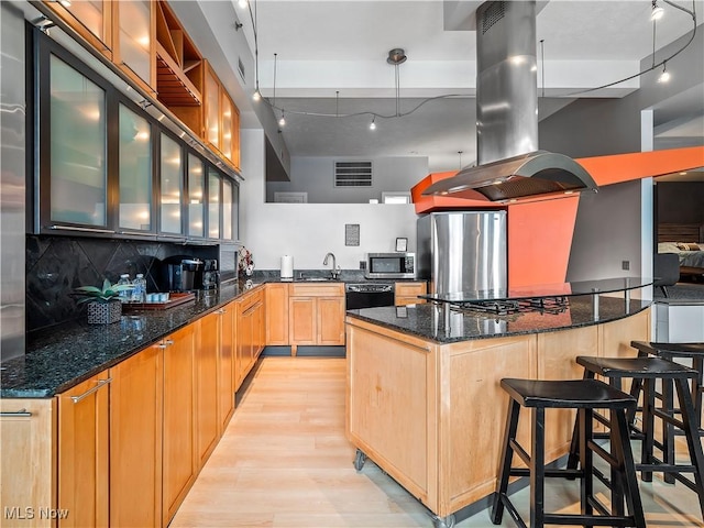 kitchen with island range hood, a sink, light wood-style floors, appliances with stainless steel finishes, and backsplash