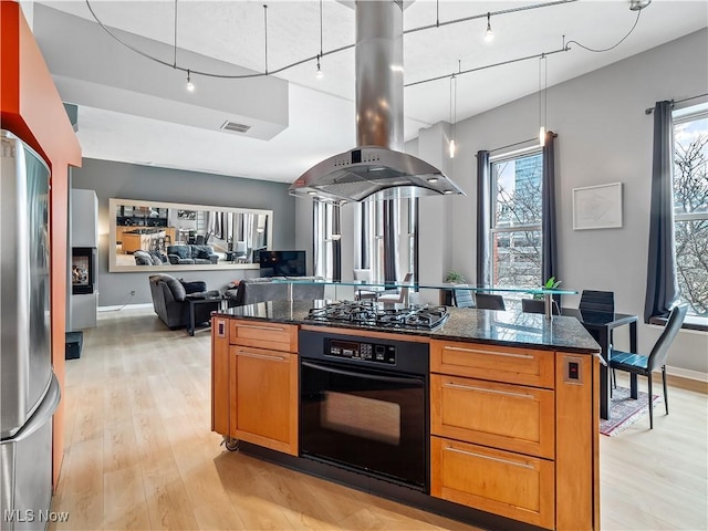 kitchen with dark stone counters, freestanding refrigerator, island exhaust hood, gas stovetop, and black oven