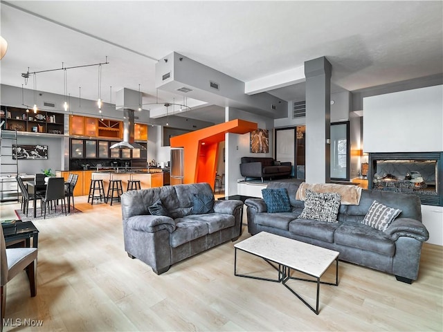 living area featuring light wood finished floors, a multi sided fireplace, and visible vents