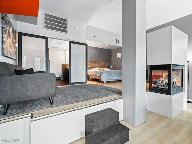 bedroom featuring a towering ceiling, visible vents, wood finished floors, and a multi sided fireplace