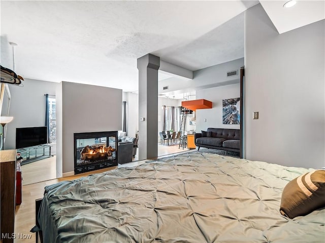 bedroom with visible vents, wood finished floors, and a multi sided fireplace