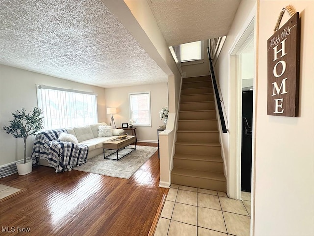 living area featuring light wood finished floors, baseboards, stairway, and a textured ceiling