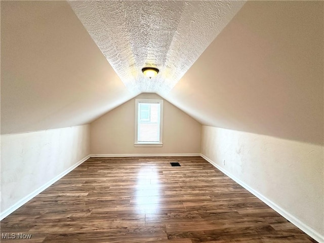 additional living space featuring lofted ceiling, a textured ceiling, baseboards, and wood finished floors