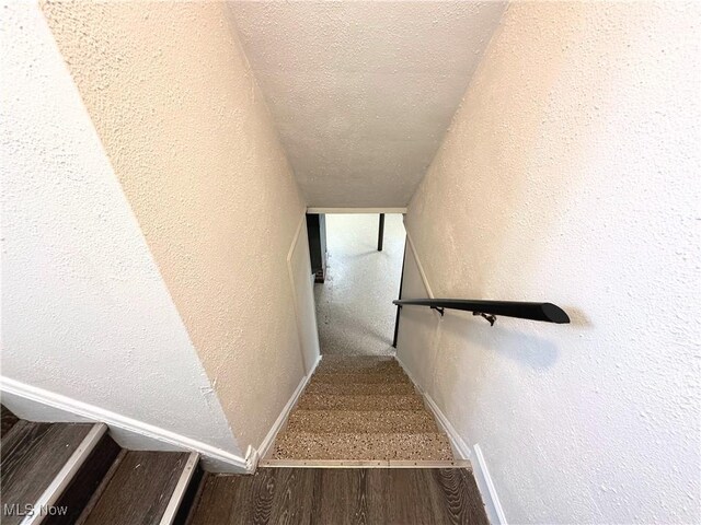 stairway with a textured wall, a textured ceiling, baseboards, and wood finished floors