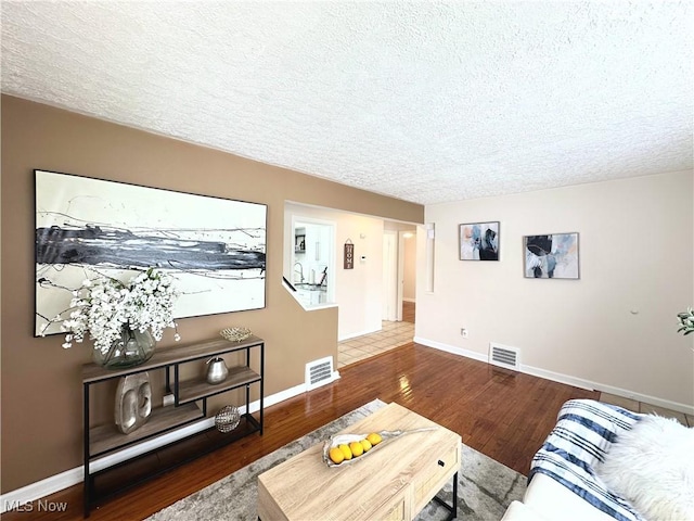 living room with a textured ceiling, visible vents, and wood finished floors