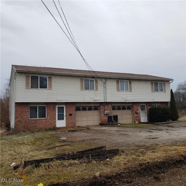 townhome / multi-family property featuring a garage, brick siding, and dirt driveway