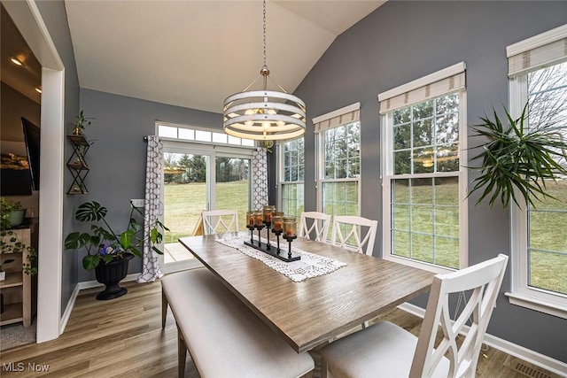 dining room featuring lofted ceiling, visible vents, wood finished floors, a chandelier, and baseboards