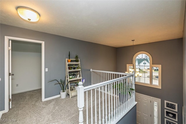 corridor featuring carpet floors, a textured ceiling, baseboards, and an inviting chandelier