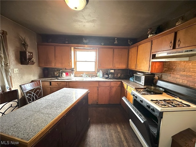 kitchen with under cabinet range hood, light countertops, brown cabinetry, white gas range, and dark wood finished floors