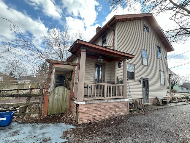 view of front facade with covered porch, a chimney, a gate, and fence