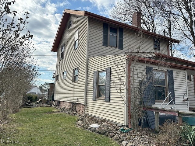 view of side of home with a chimney and a yard