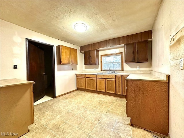 kitchen with a textured ceiling, light countertops, brown cabinetry, and a sink