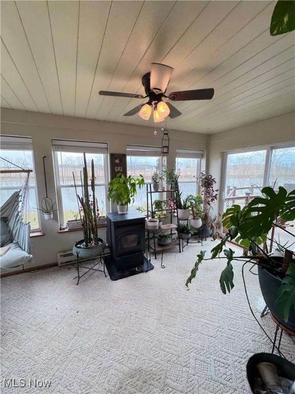 unfurnished sunroom with a ceiling fan, wooden ceiling, and a wood stove