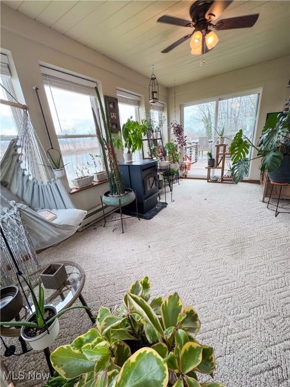 sunroom / solarium with ceiling fan and a wood stove