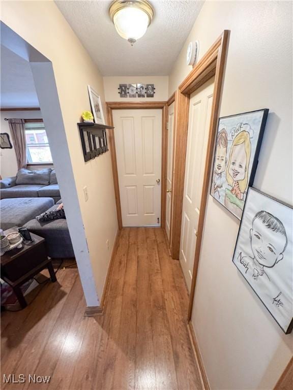 hallway featuring light wood finished floors, a textured ceiling, and baseboards