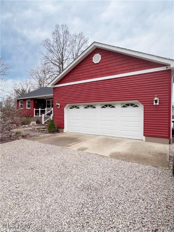 ranch-style house with gravel driveway, covered porch, and a garage
