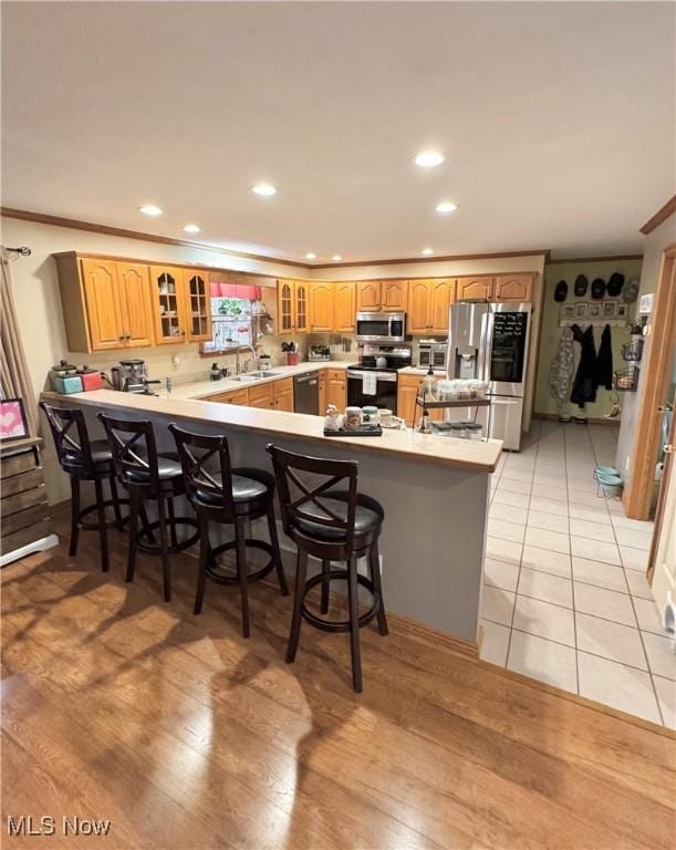 kitchen with a kitchen bar, glass insert cabinets, appliances with stainless steel finishes, and a peninsula