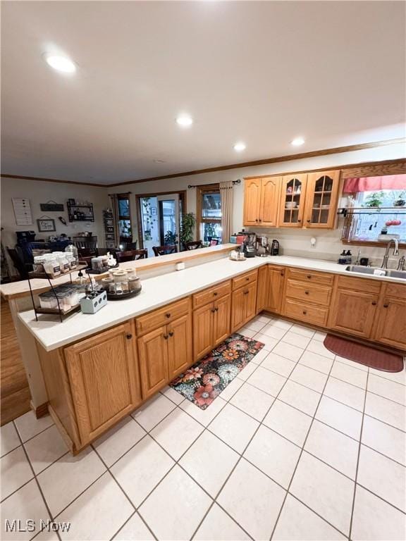 kitchen featuring glass insert cabinets, light countertops, a peninsula, light tile patterned flooring, and a sink