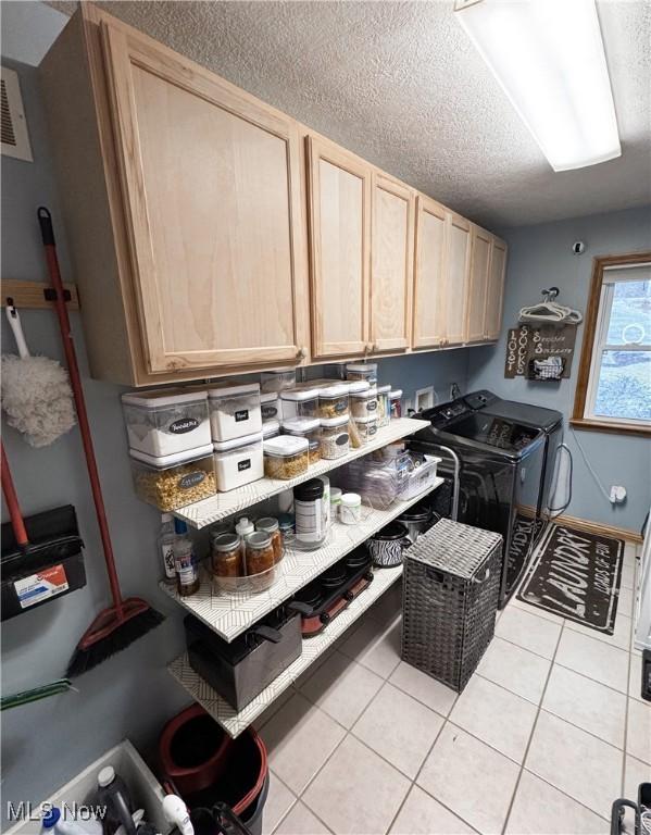laundry area featuring light tile patterned floors, independent washer and dryer, a textured ceiling, and cabinet space