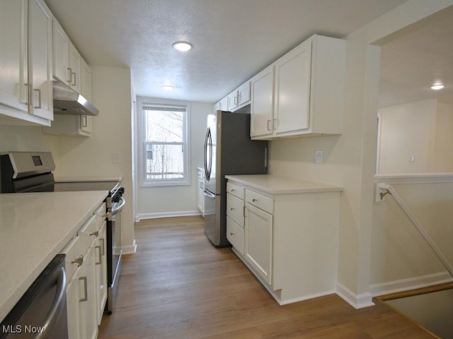 kitchen with stainless steel appliances, light countertops, white cabinets, and under cabinet range hood