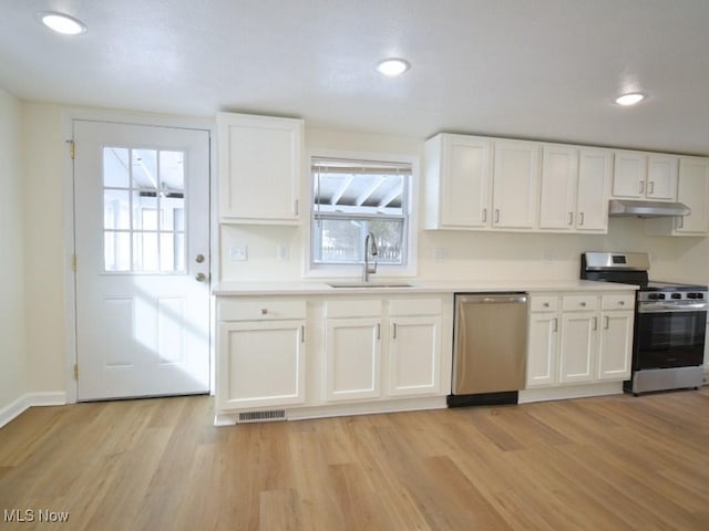 kitchen featuring light wood-style flooring, under cabinet range hood, stainless steel appliances, a sink, and white cabinetry