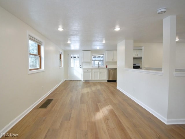 unfurnished living room featuring light wood-style floors, visible vents, a sink, and baseboards