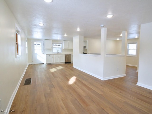 unfurnished living room featuring light wood-type flooring, visible vents, a sink, and baseboards