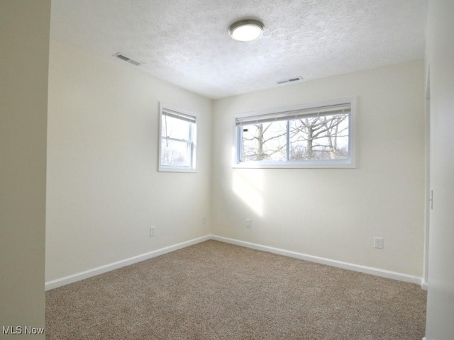 carpeted empty room featuring a textured ceiling, visible vents, and baseboards