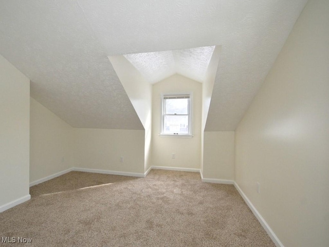 additional living space with lofted ceiling, light carpet, a textured ceiling, and baseboards