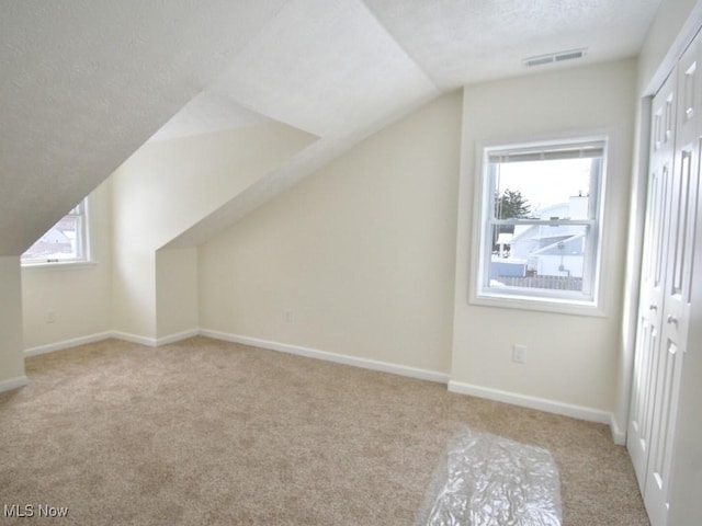 bonus room featuring a textured ceiling, lofted ceiling, visible vents, baseboards, and carpet