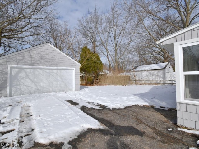 yard covered in snow featuring an outbuilding, fence, and a detached garage